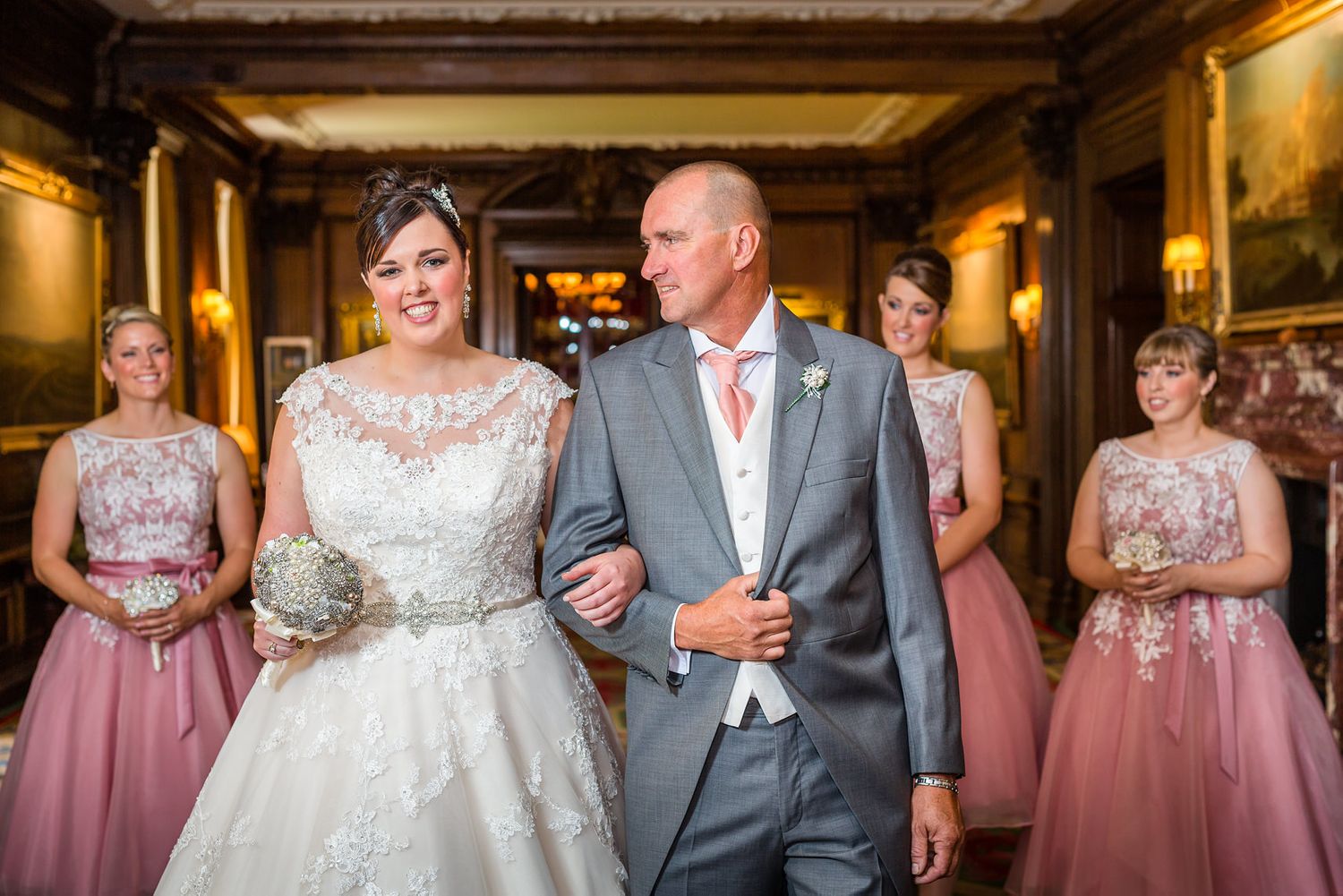 Wedding party walking through an ornate hallway with bridesmaids in pink dresses.