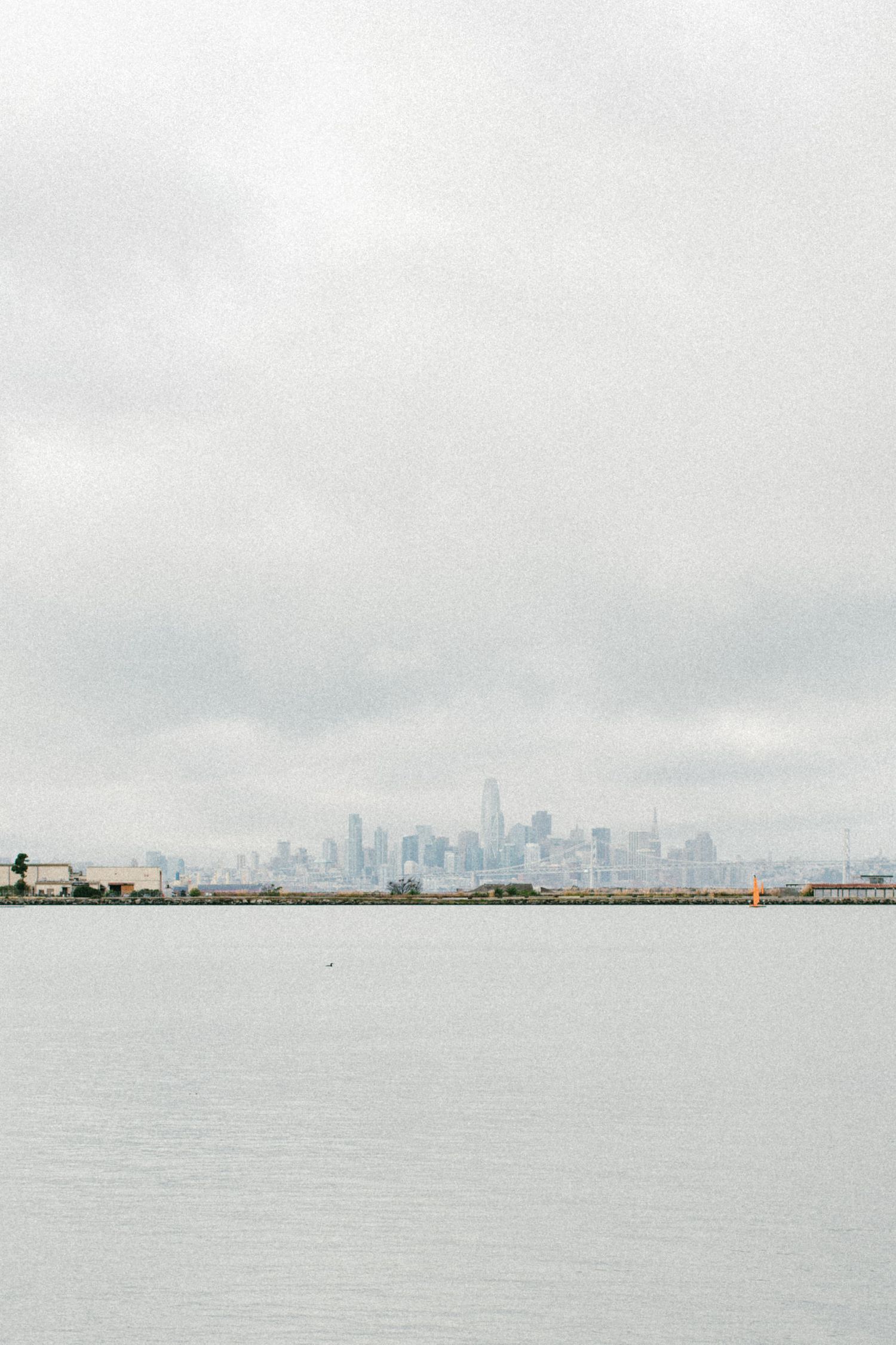Foggy cityscape view of downtown buildings across a gray harbor.