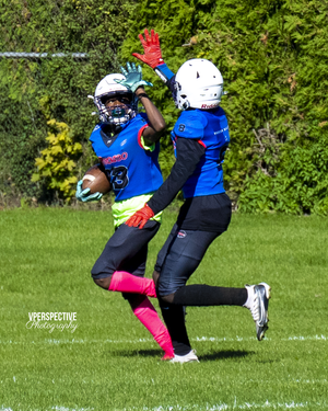 Two football players in blue uniforms compete for the ball during game action on grass field.