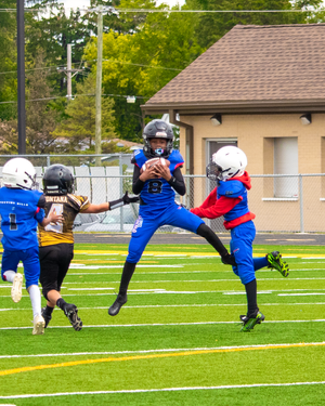 Football players leap high in the air during game action on artificial turf field.