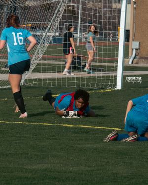 Soccer players near a goal net during an intense game moment with a diving save.