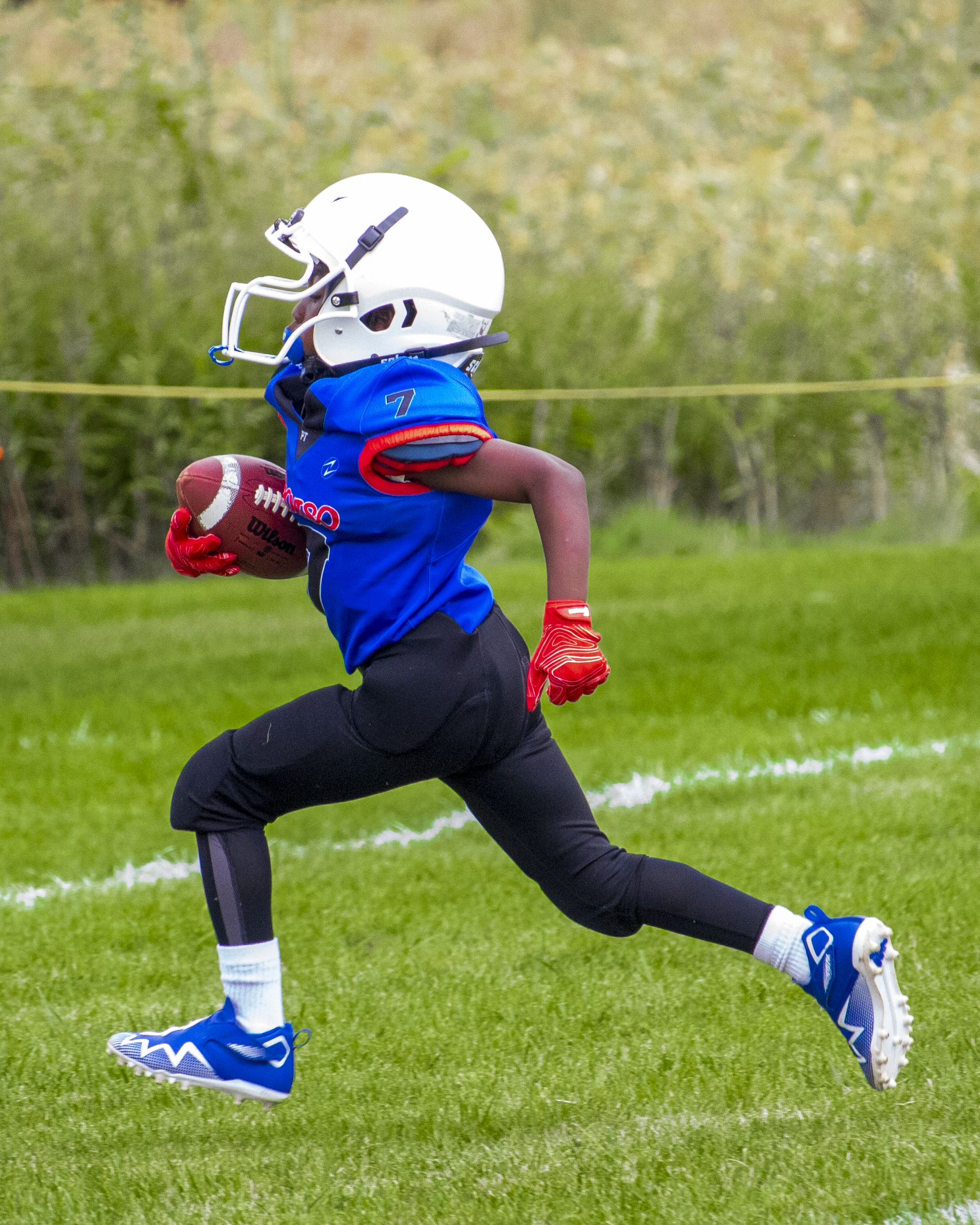 Youth football player in blue uniform running with ball during game.