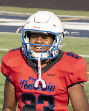 Football player wearing white helmet and red jersey on sports field.