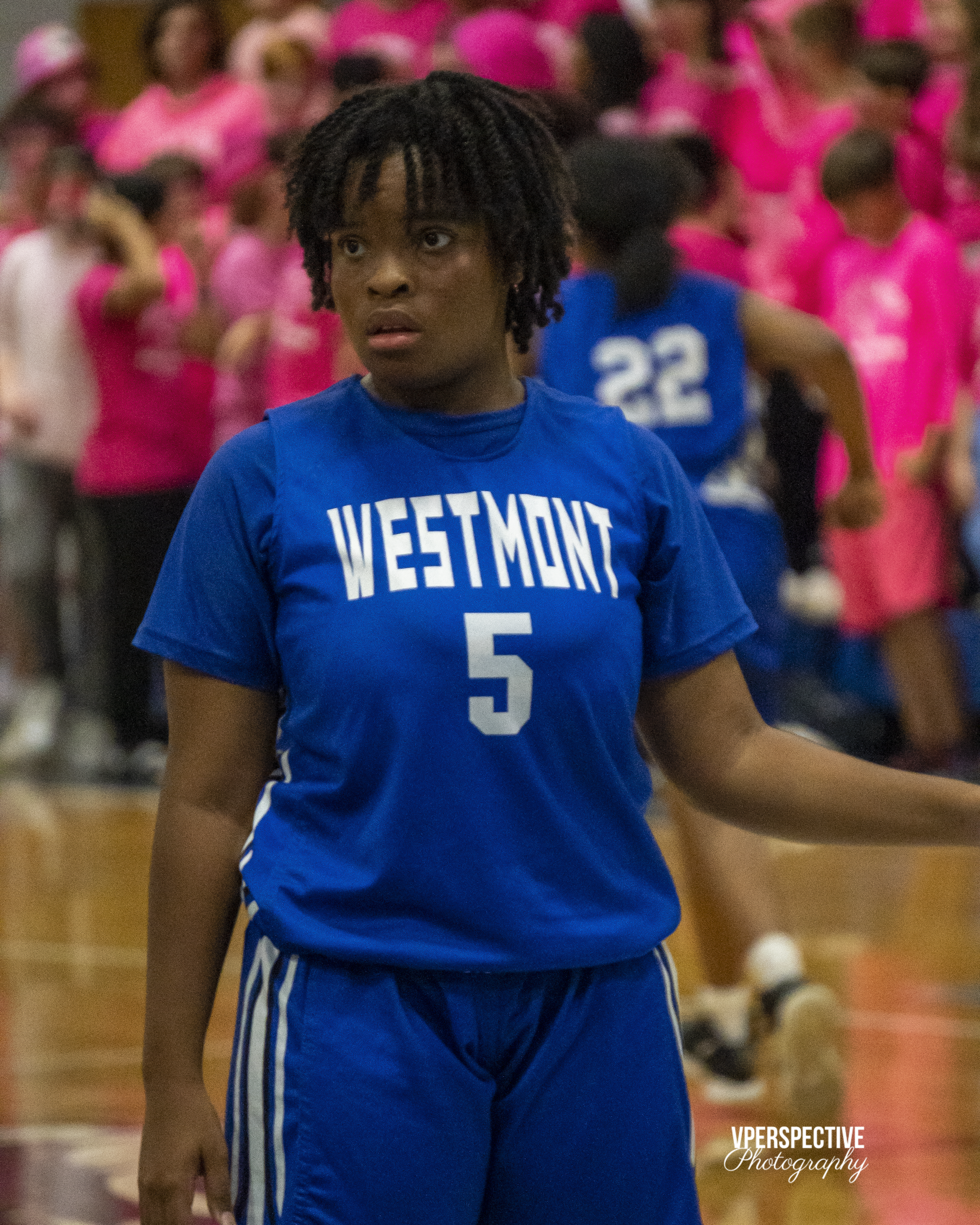 Basketball player wearing blue Westmont jersey number 5 stands on indoor court.