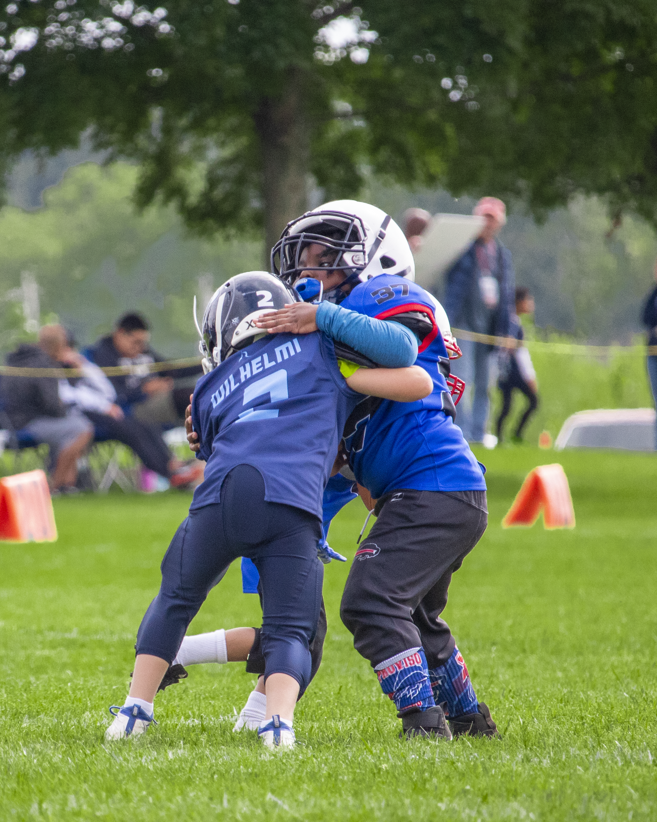 Youth football players in blue uniforms practicing blocking drills on field.