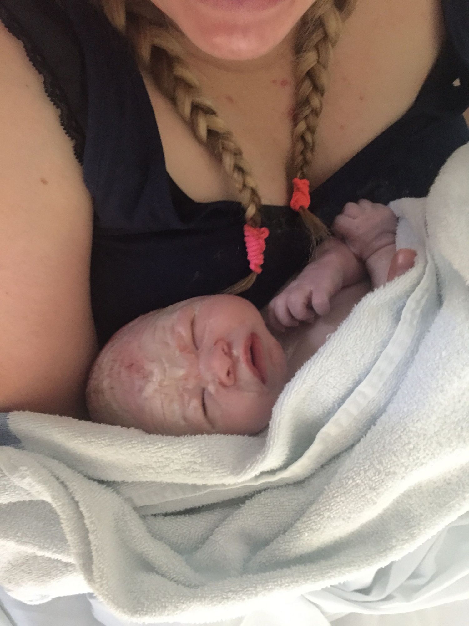 Sleeping newborn wrapped in white blanket resting against caregiver.