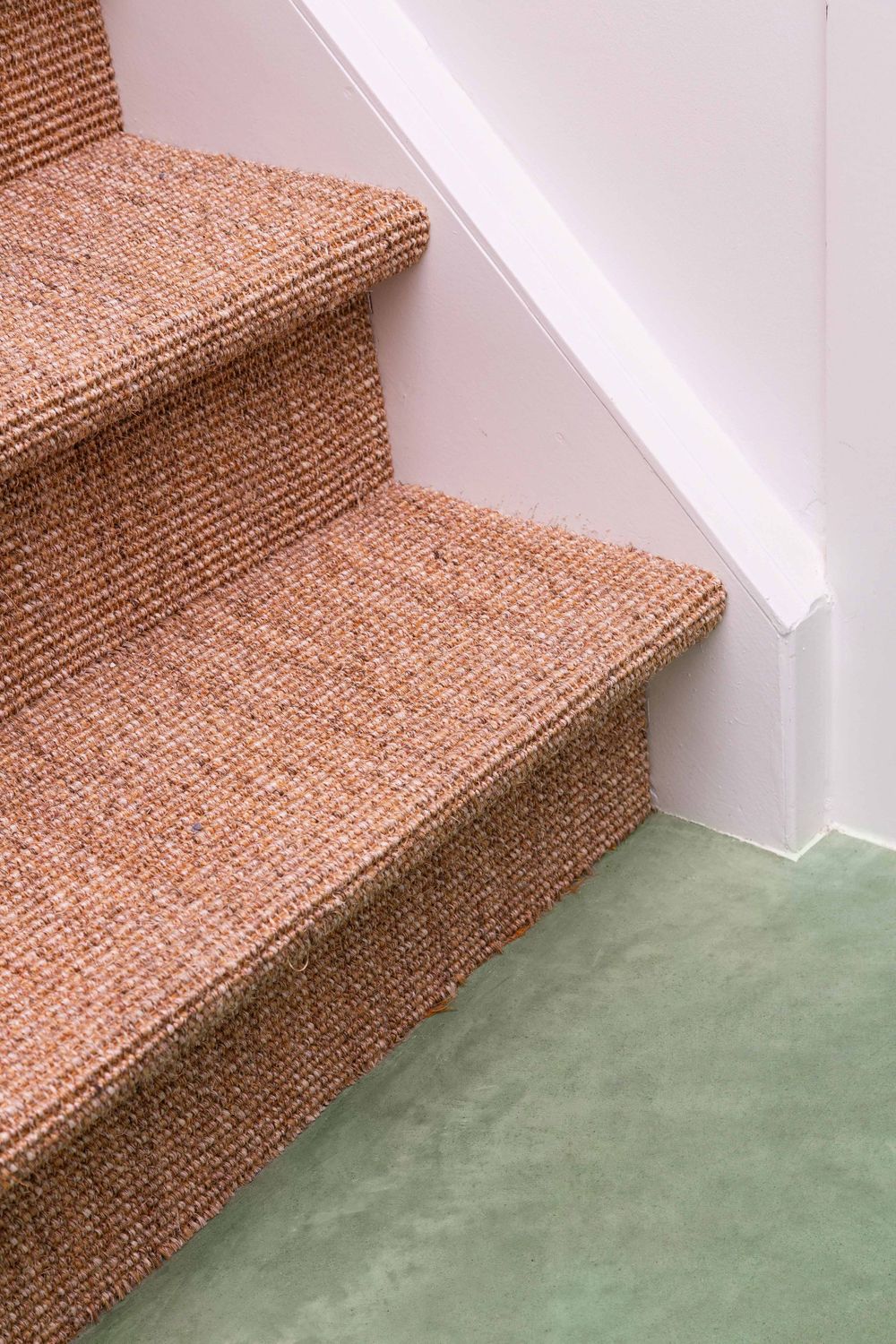 Textured brown carpet stairs meeting mint green flooring in minimalist interior.