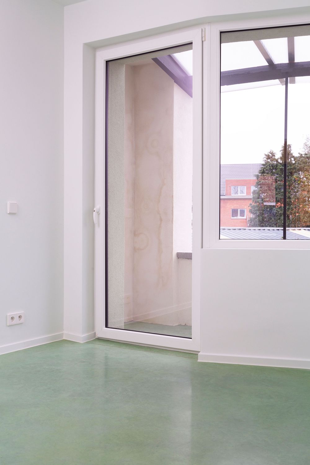 Empty modern room with large windows, white walls, and mint green concrete floor.