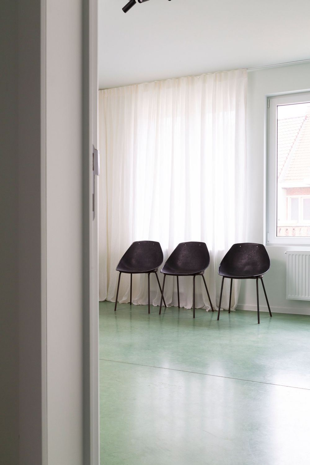 Modern interior space with black chairs against white walls and mint green flooring.