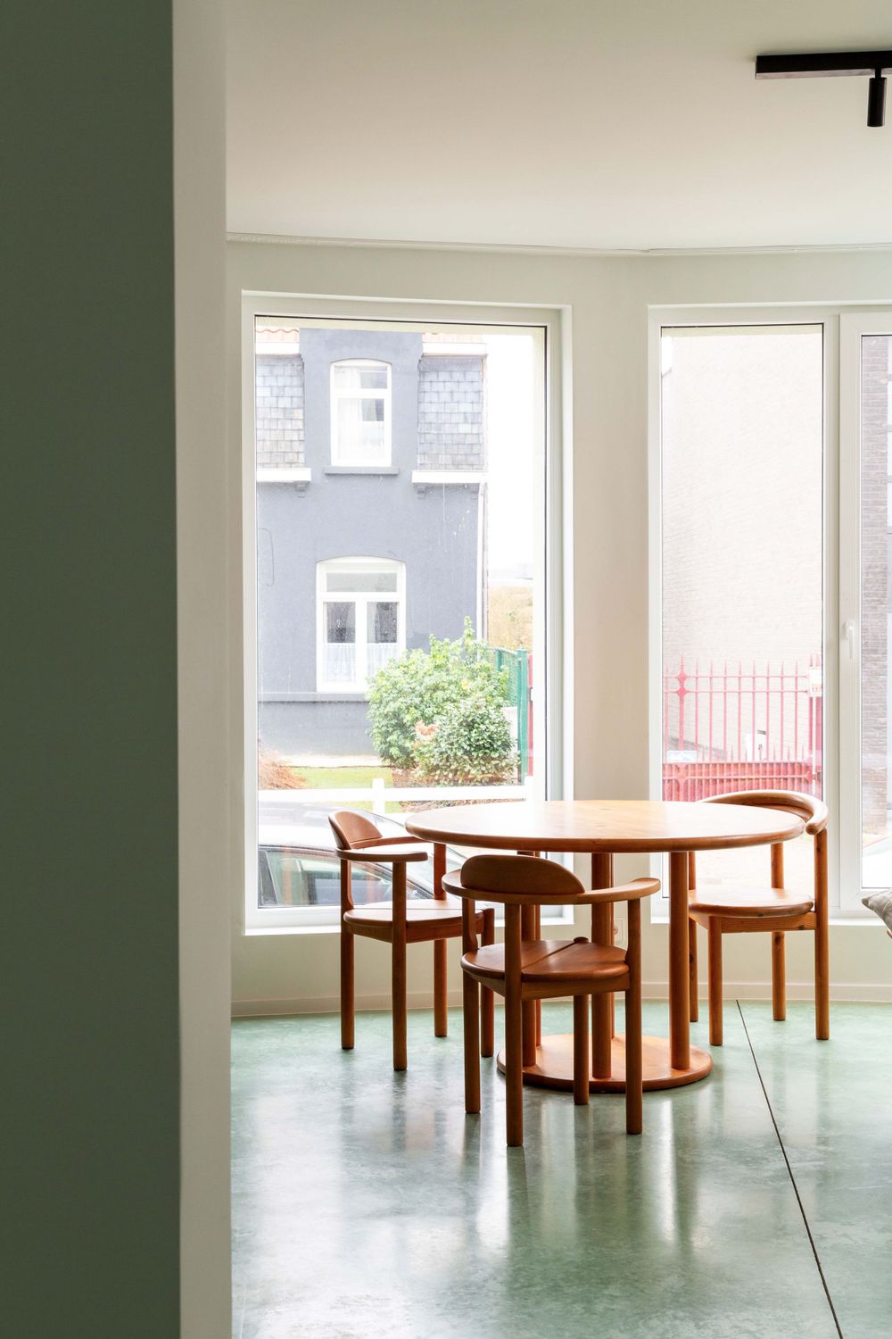 Minimalist room with wooden tables and chairs on mint green polished concrete floor.