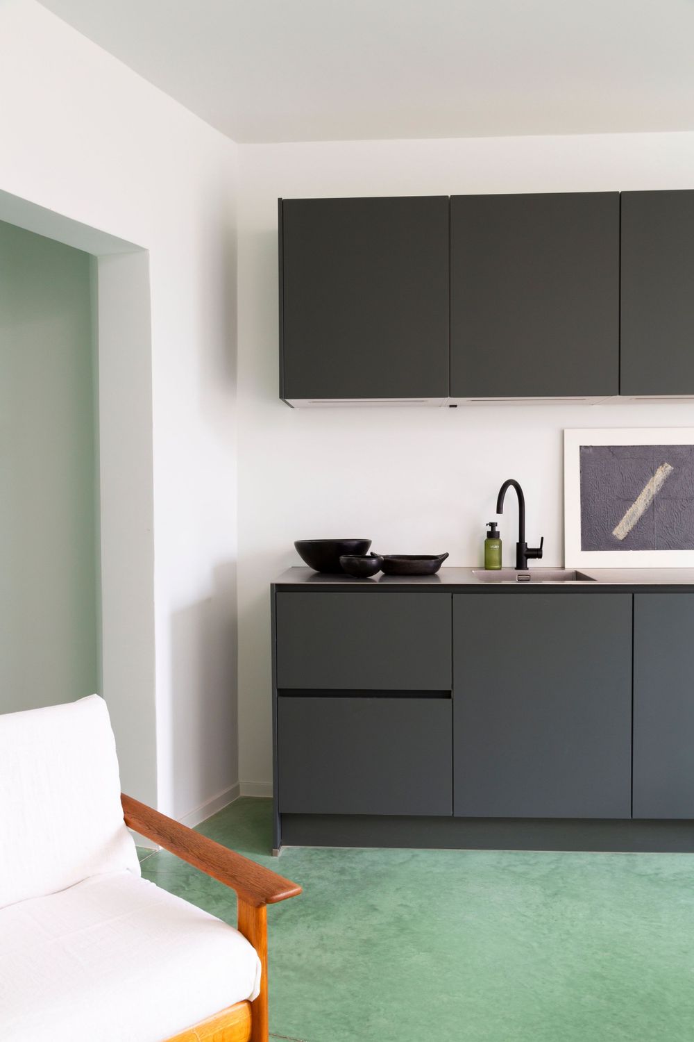 Modern black kitchen cabinets mounted on white wall with mint green floor.