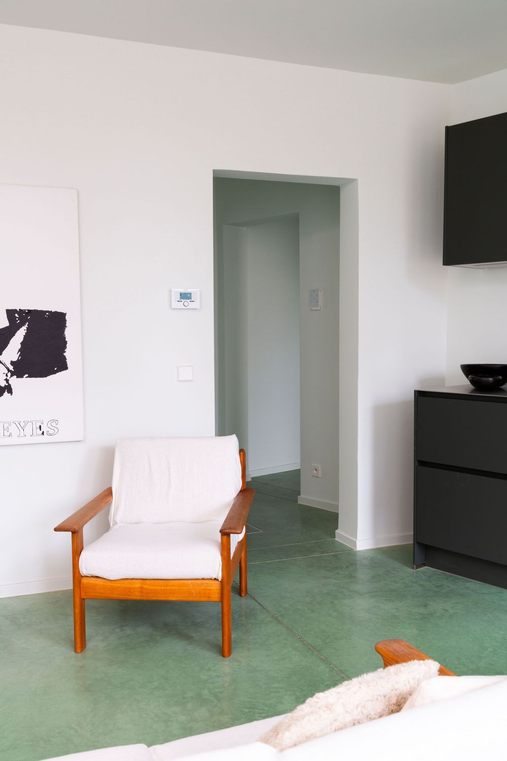 Minimalist living area with orange accent chair and black kitchen cabinets against white walls.