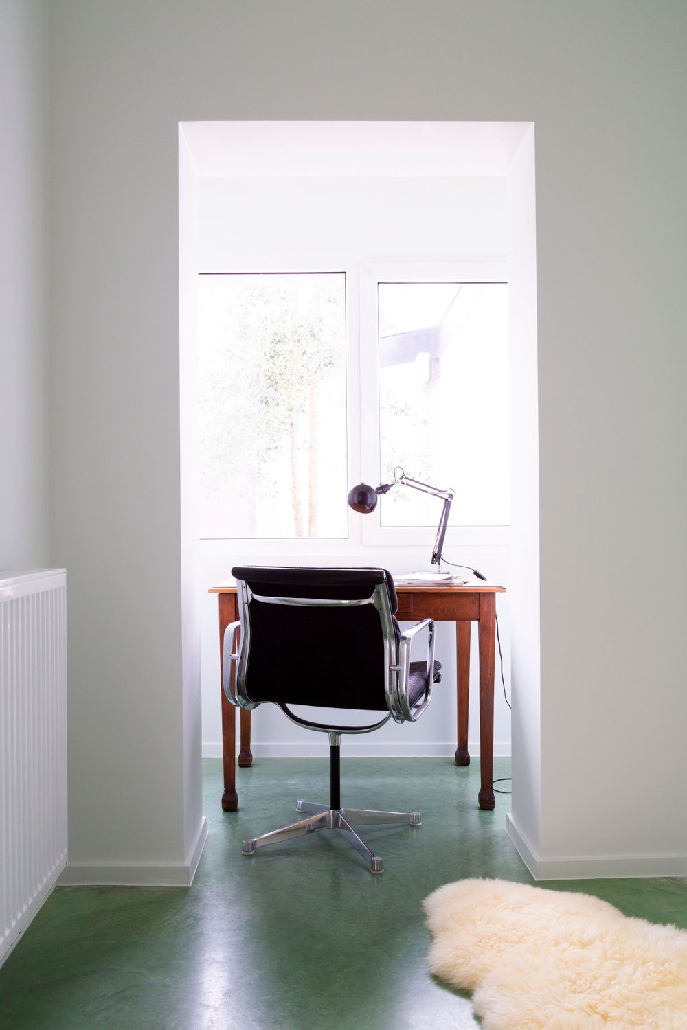 Modern office setup with wooden desk and black chair on mint green flooring.