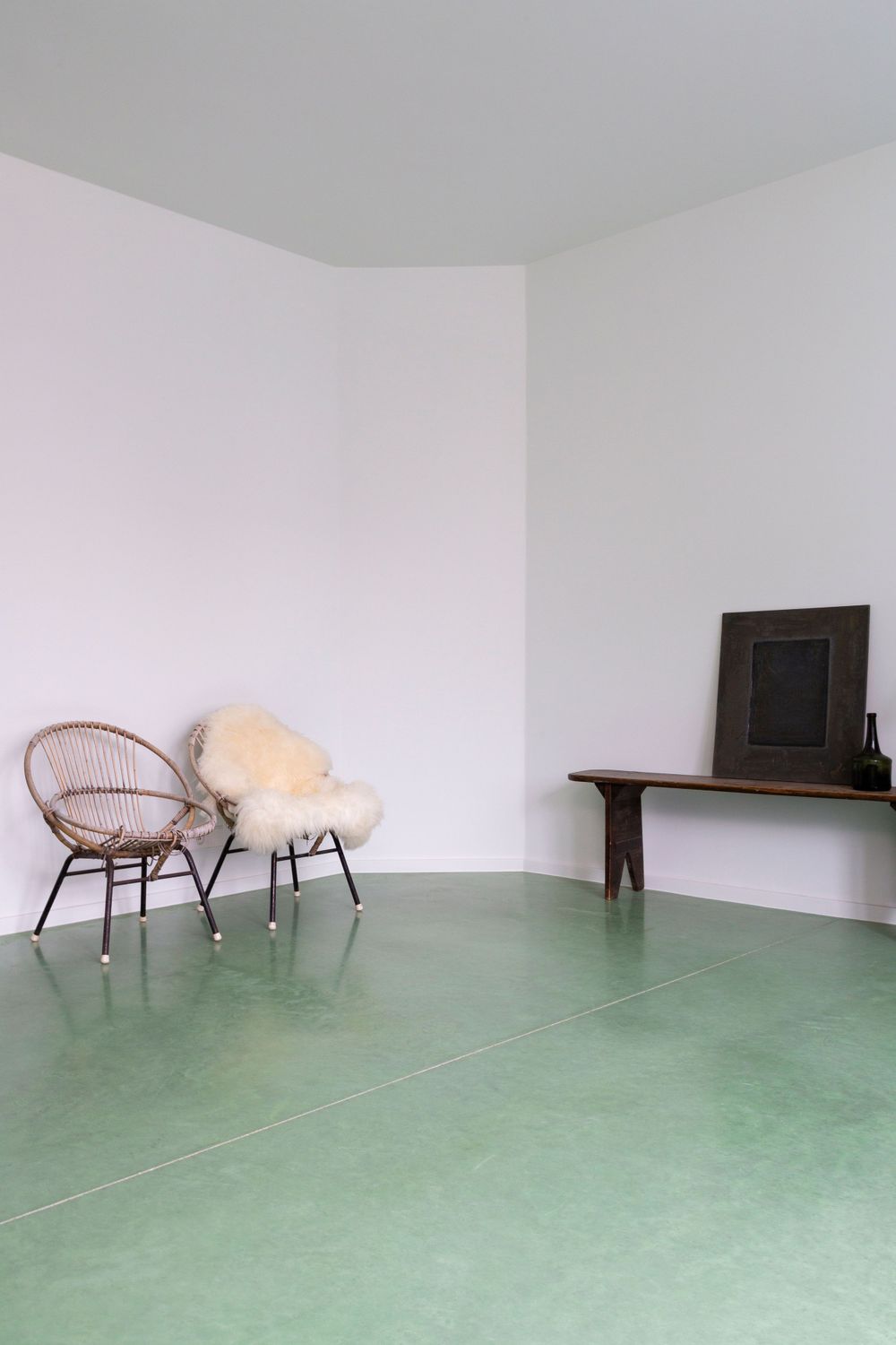 Modern living space with rattan chairs and green flooring against white walls.