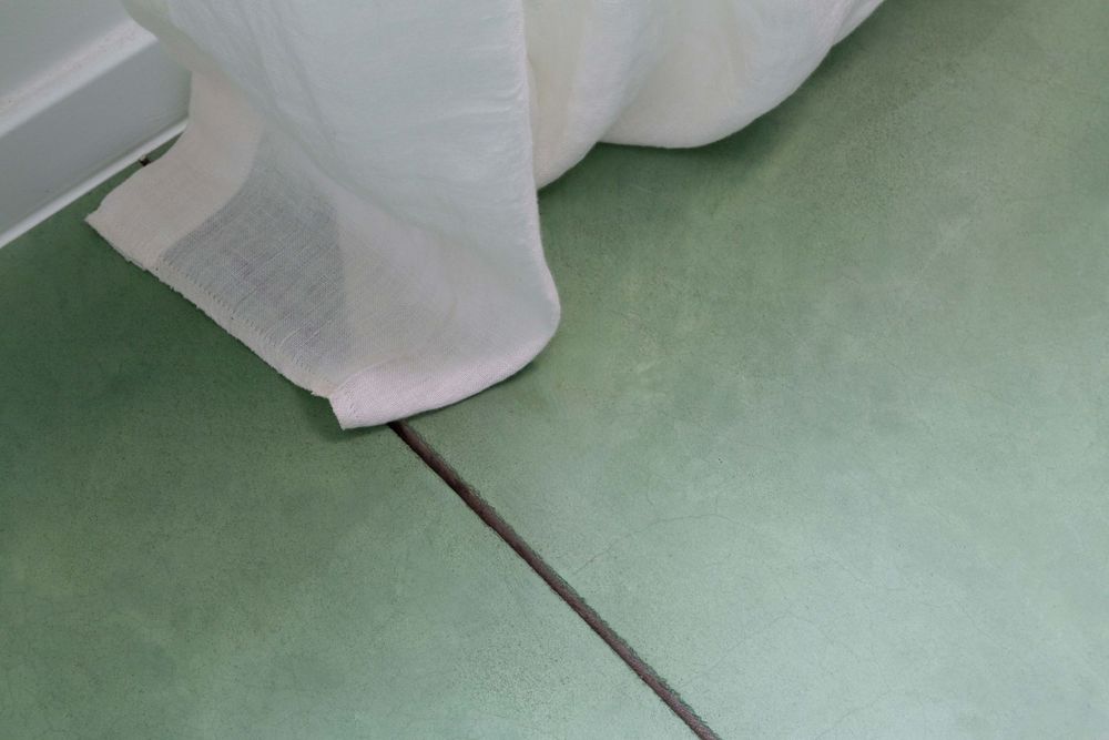 Abstract view of white curtains draping against mint green floor.