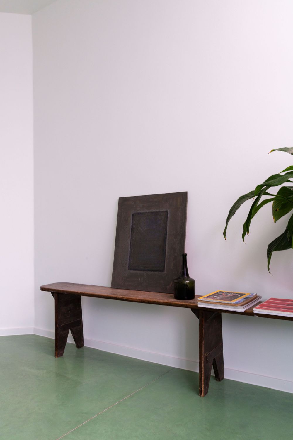 Wooden bench with dark panels mounted along white wall on green flooring.