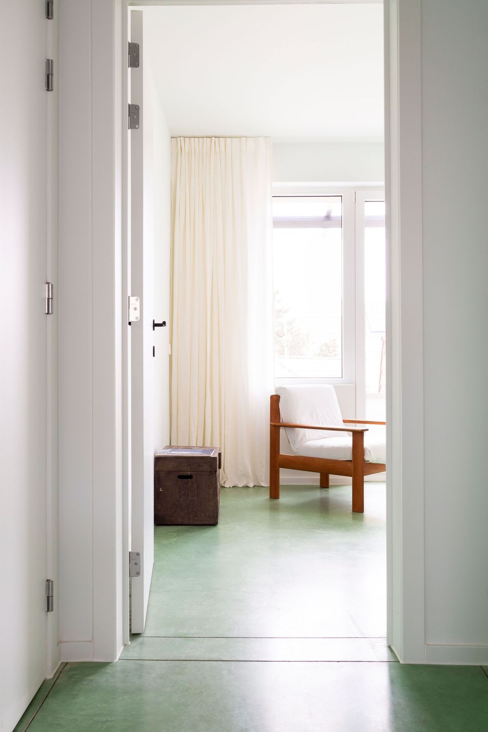 Long hallway with white walls, mint green floor, and natural light streaming through doorways.