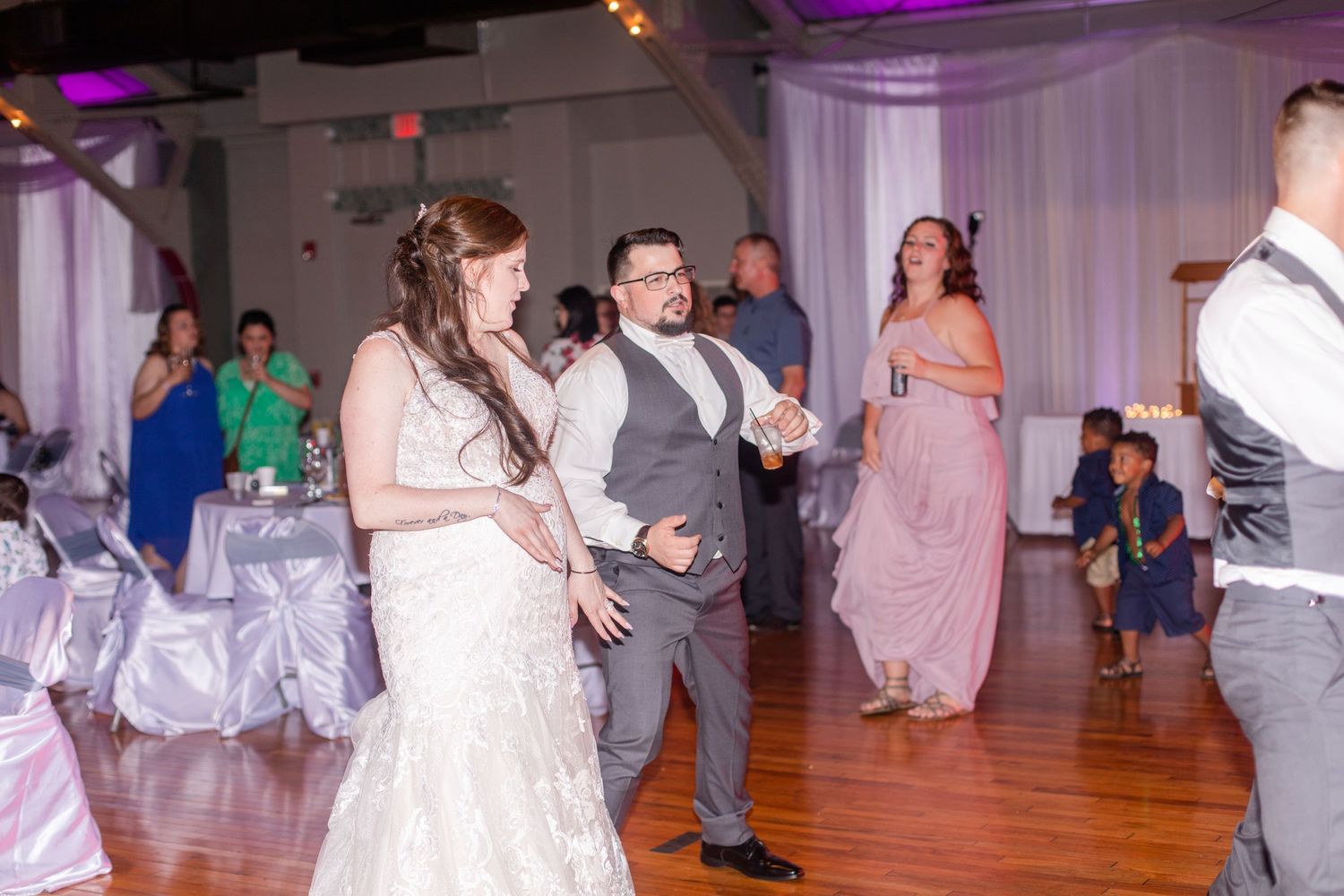 Wedding reception dance floor filled with guests celebrating under purple lighting.