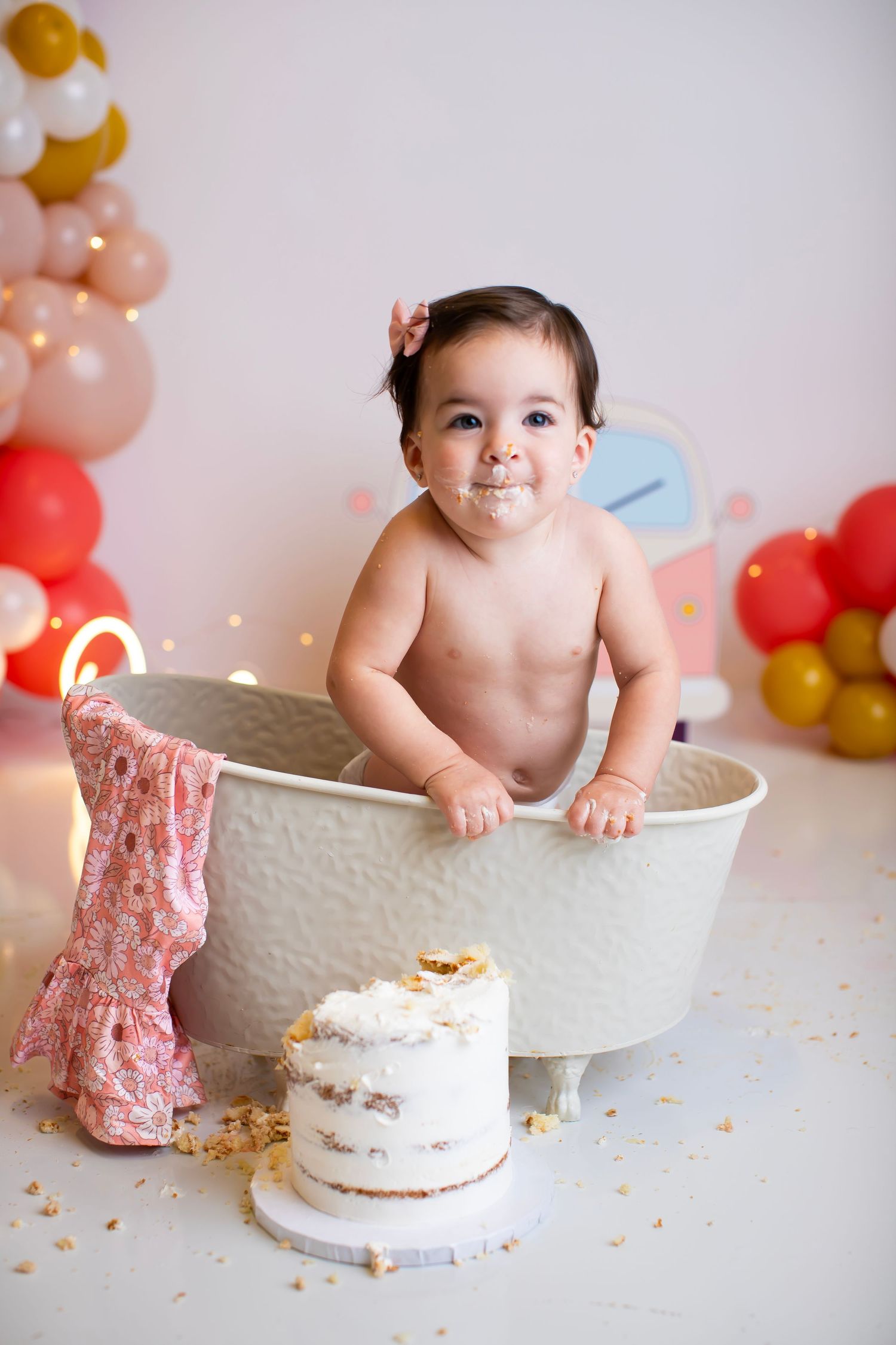 White bathtub setup for cake smash photo session with colorful balloon decorations.