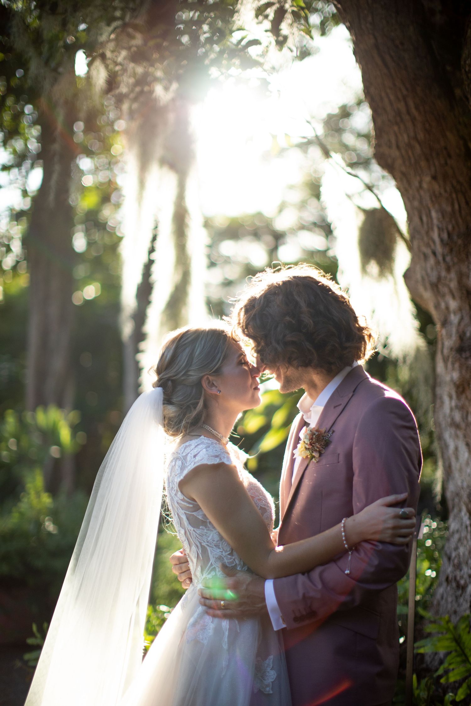 Romantic sunset wedding portrait of couple embracing among trees with beautiful backlighting.