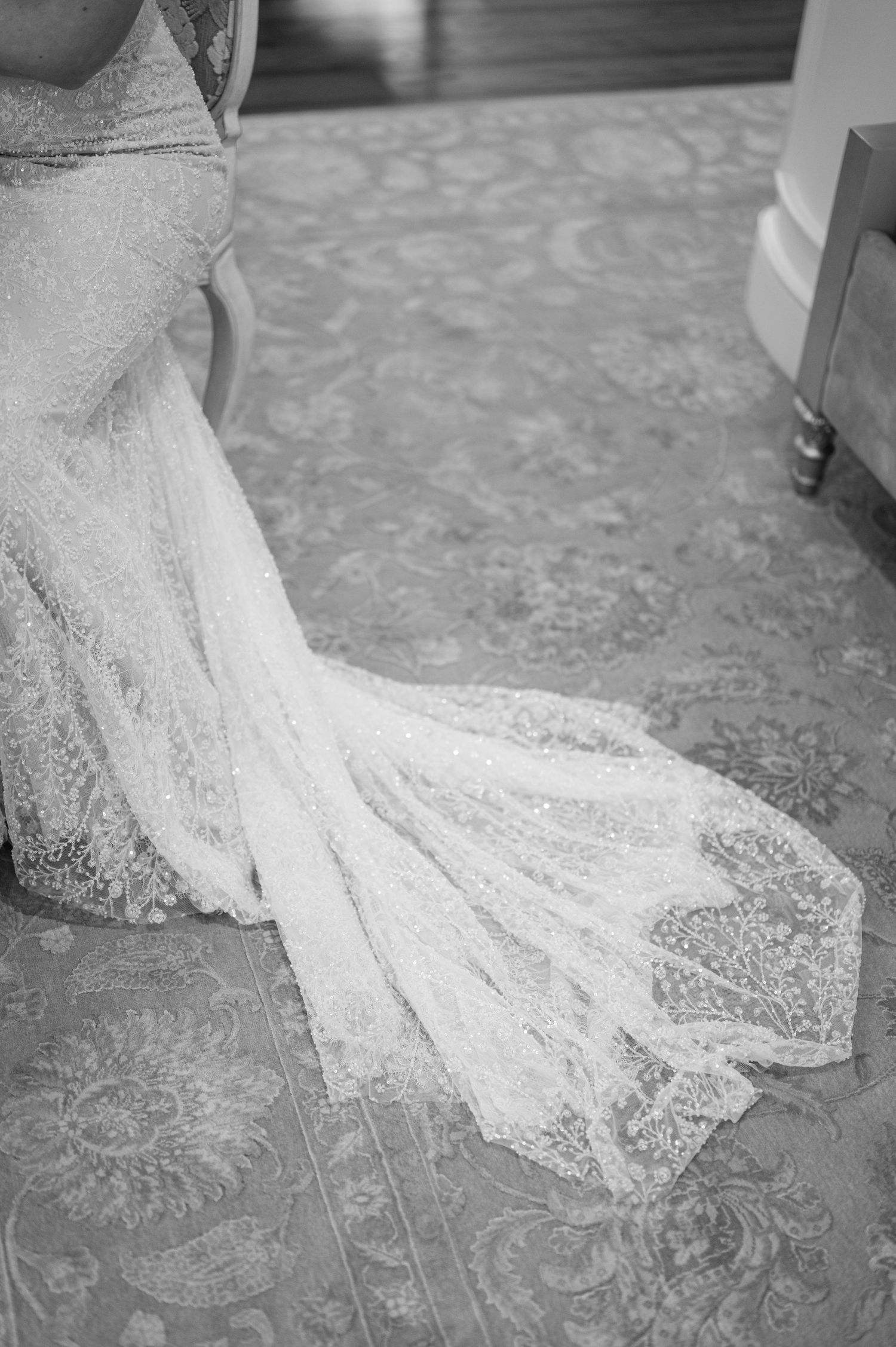 Close-up of lace wedding dress train flowing across patterned floor.