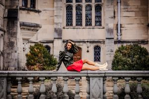 trendy and cool, this girl wears a leather jacket and sits on a stone railing