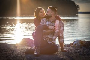 The setting sun glistens off of the lake behind this engaged couple who look at each other compassionately.
