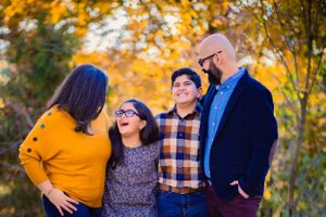 A colorful picture taken of a family among fall leaves. The family is laughing at each other and having fun