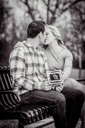A husband and wife steal a kiss while sharing a picture of the sonogram