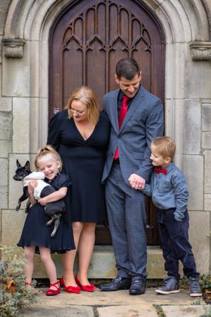 A mother and father hold their young children's hands and laugh as the girl struggles to hold the small dog