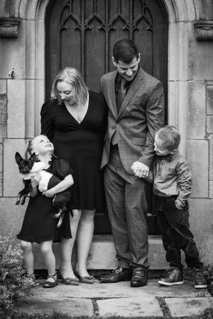 A mother and father hold their young children's hands and laugh as the girl struggles to hold the small dog