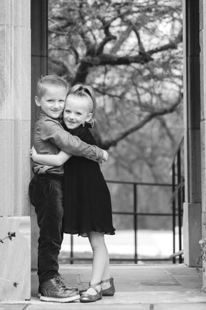 Twin brother and sister steal a big hug underneath a stone archway