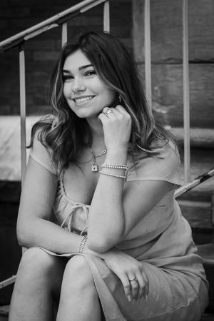 A black and white senior picture of a girl sitting and smiling off camera