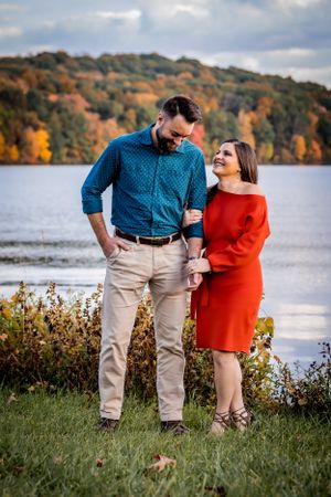 A stylish engaged couple laugh heartily while a pristine lake spreads behind them