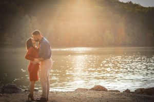 An engaged couple make the most of the setting sun and pristine lake to engage in a passionate a kiss