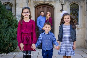 3 children dressed in fancy clothes hold hands while their parents stand behind them smiling