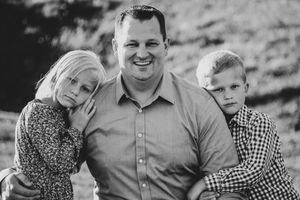 a father poses with his children who have their heads rested on his shoulders