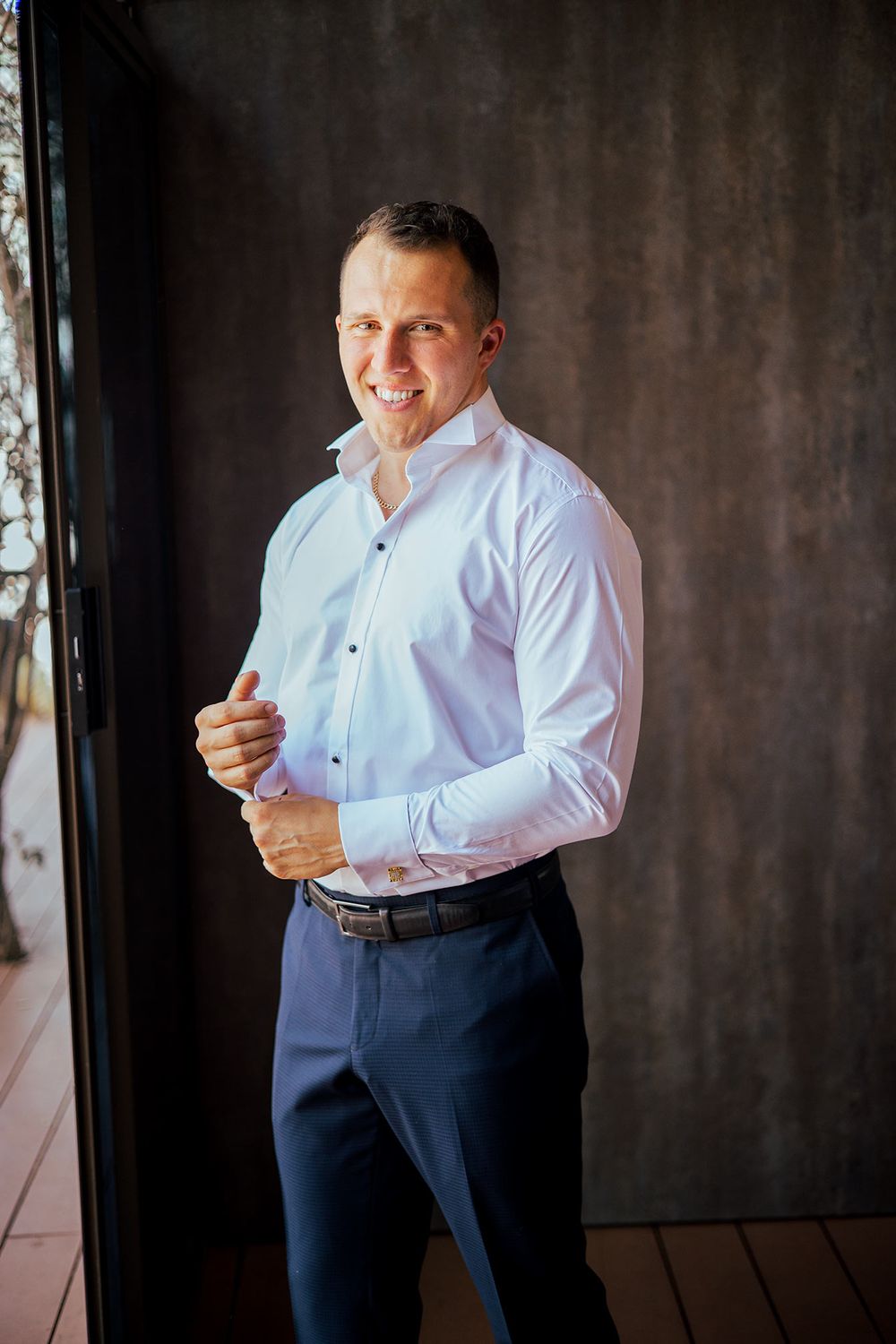 A smartly dressed person in a crisp white shirt and navy pants adjusts their cuffs.