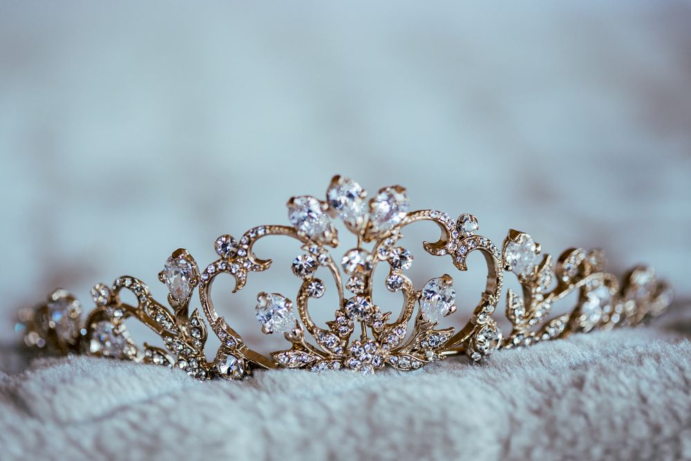 An ornate crystal and gold wedding tiara displayed against a light textured background.