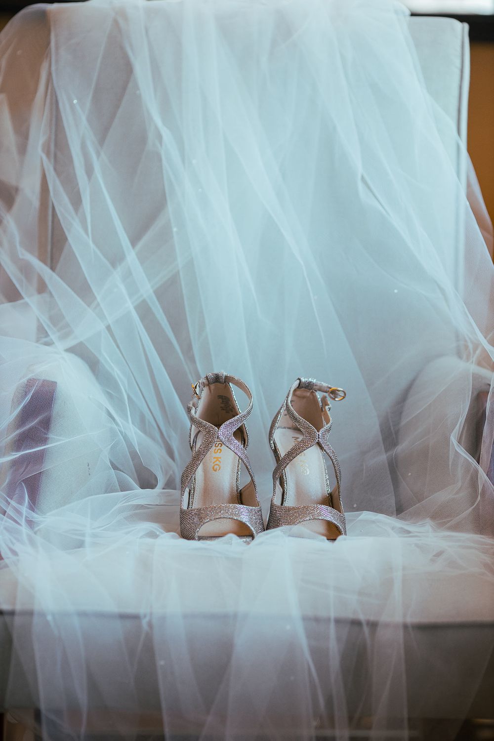 Elegant silver bridal heels displayed artistically through flowing white wedding veil material.