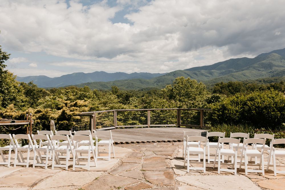 Elegant outdoor wedding ceremony setup with white chairs on a stone patio overlooking stunning mountain views.