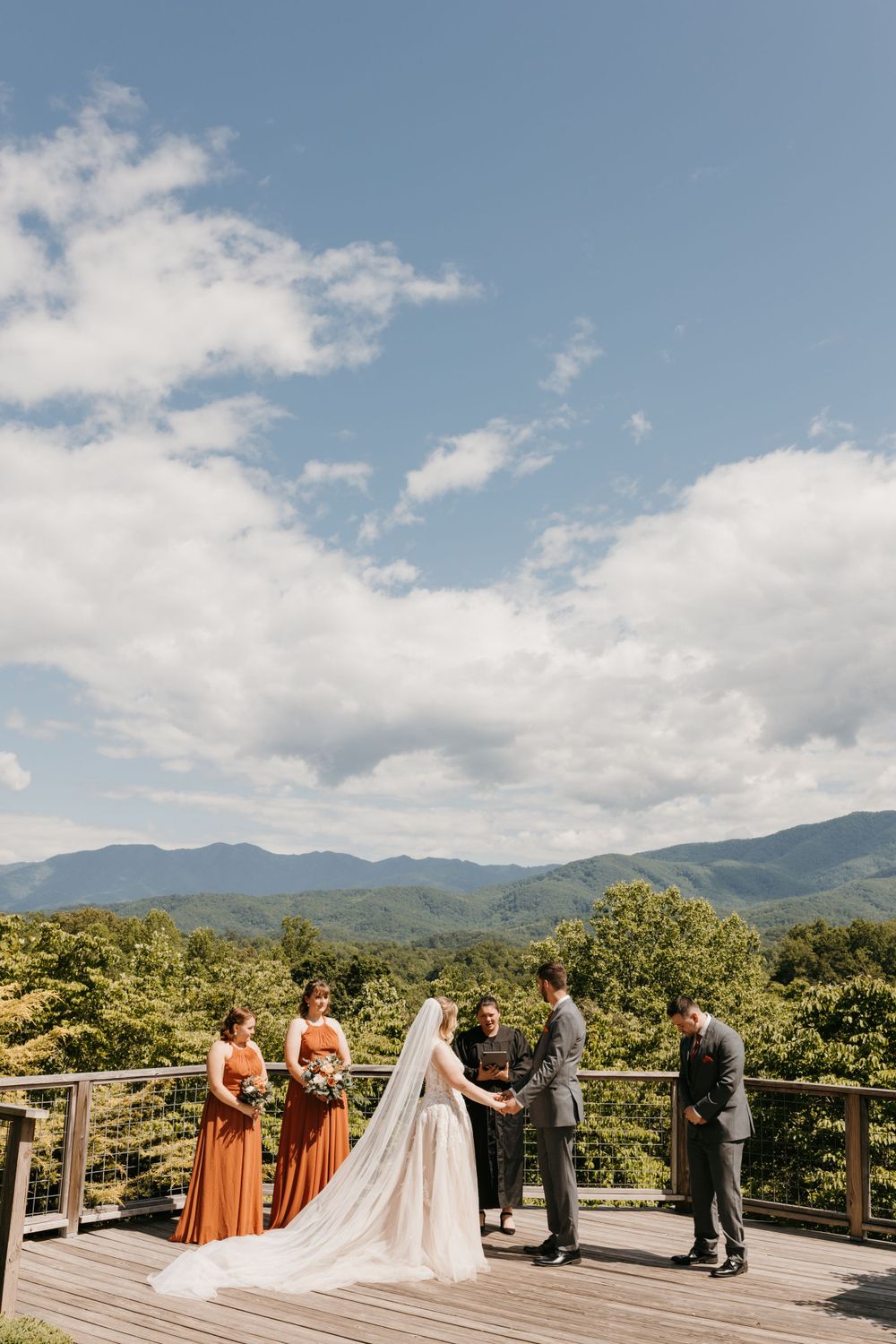 Small intimate wedding ceremony on a mountain overlook deck with bridesmaids in rust orange dresses and blue skies.