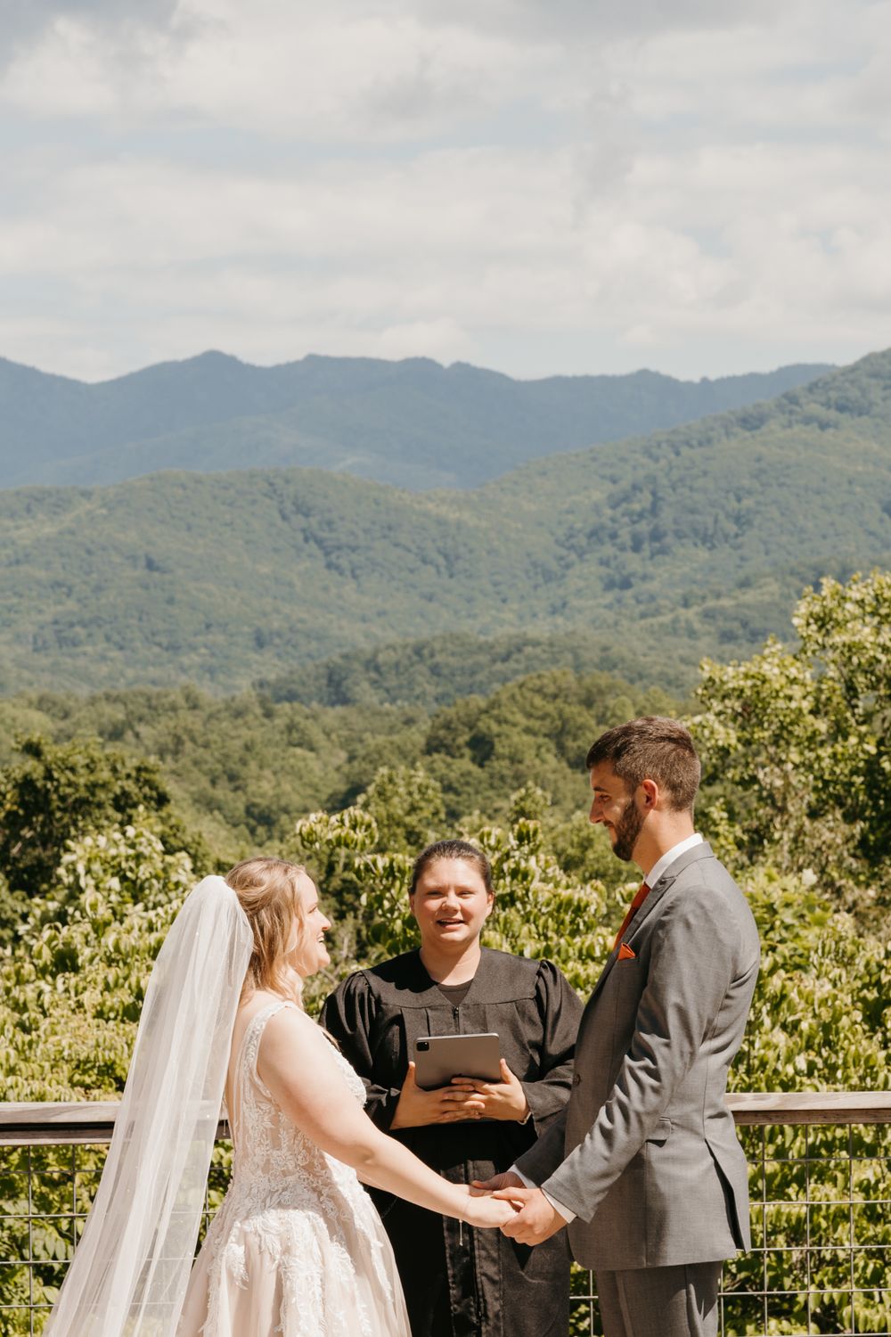 Bride and groom hold hands during outdoor wedding ceremony with stunning mountain backdrop and officiant.