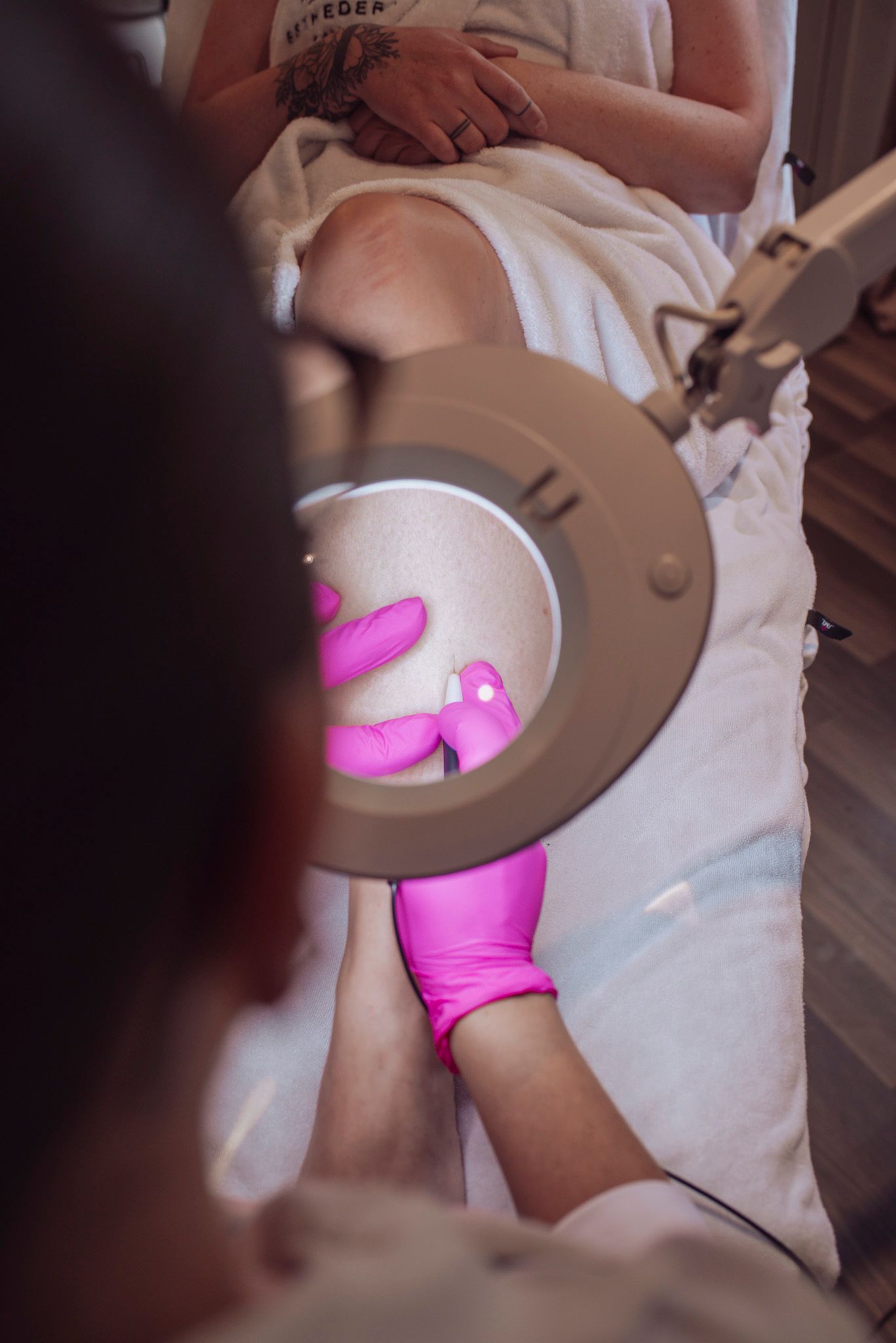 Hands wearing pink gloves performing a cosmetic treatment with specialized equipment.