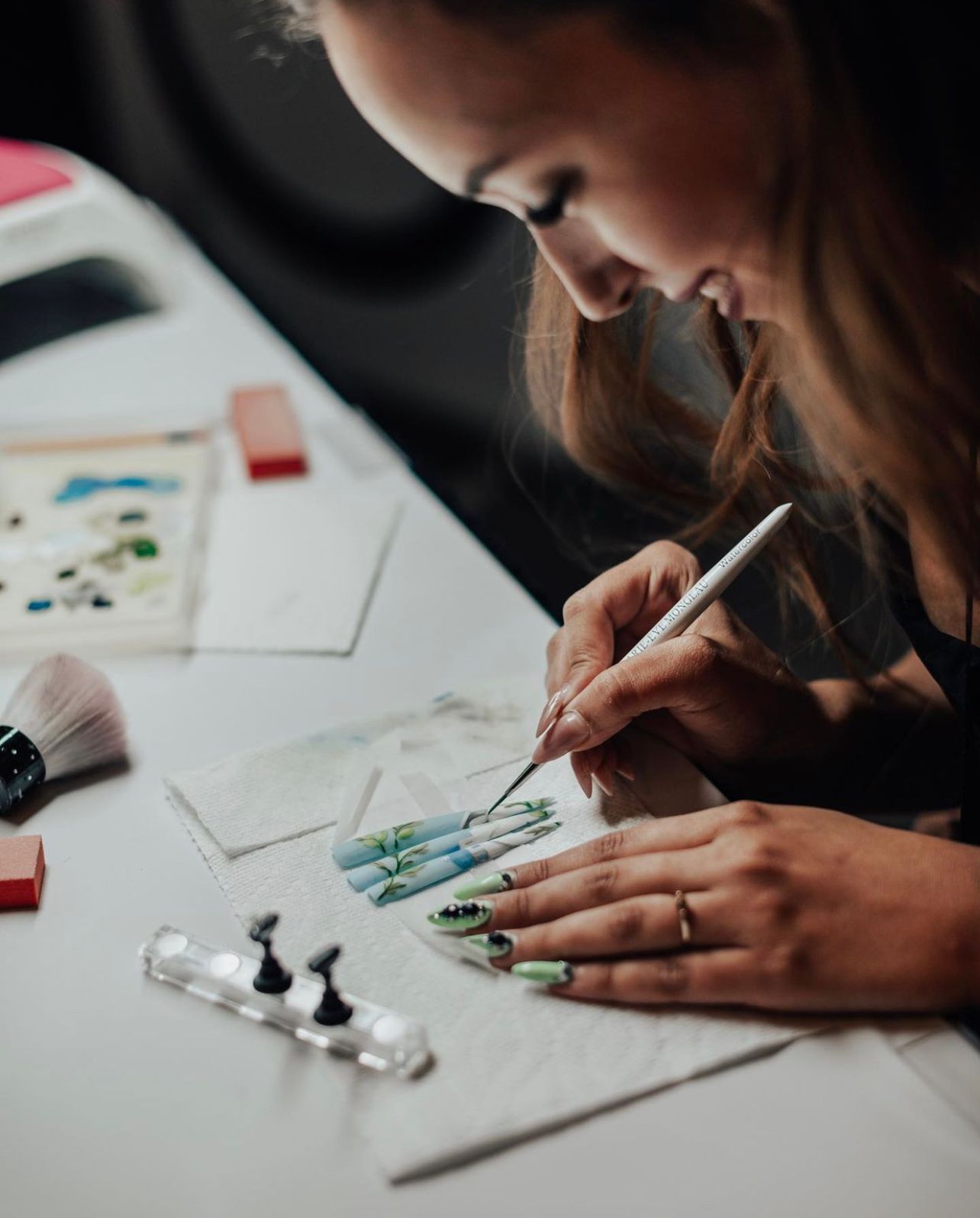 Artist working on detailed illustrations at white desk with art supplies.