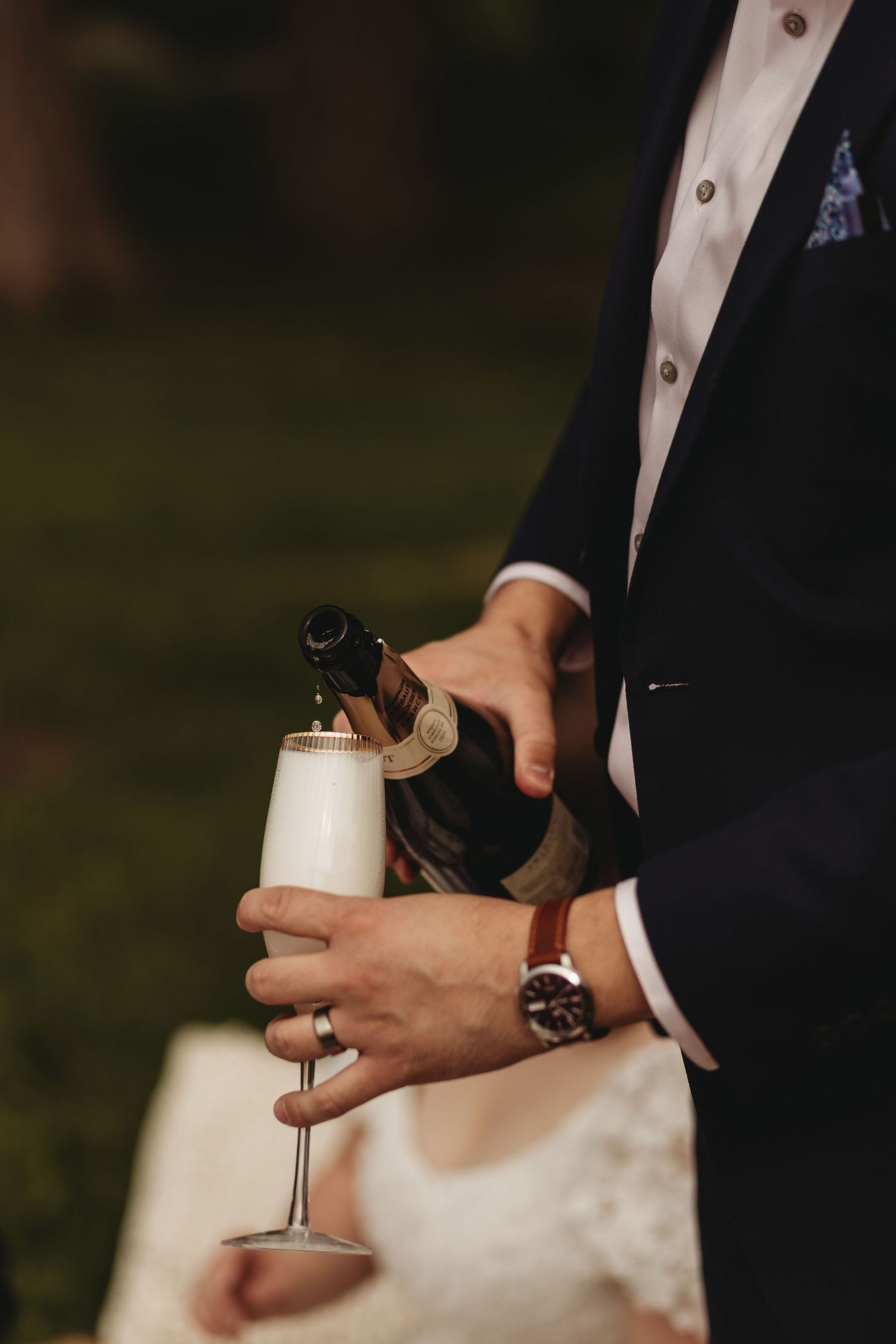 Hands holding a champagne bottle and glass during an elegant outdoor celebration.