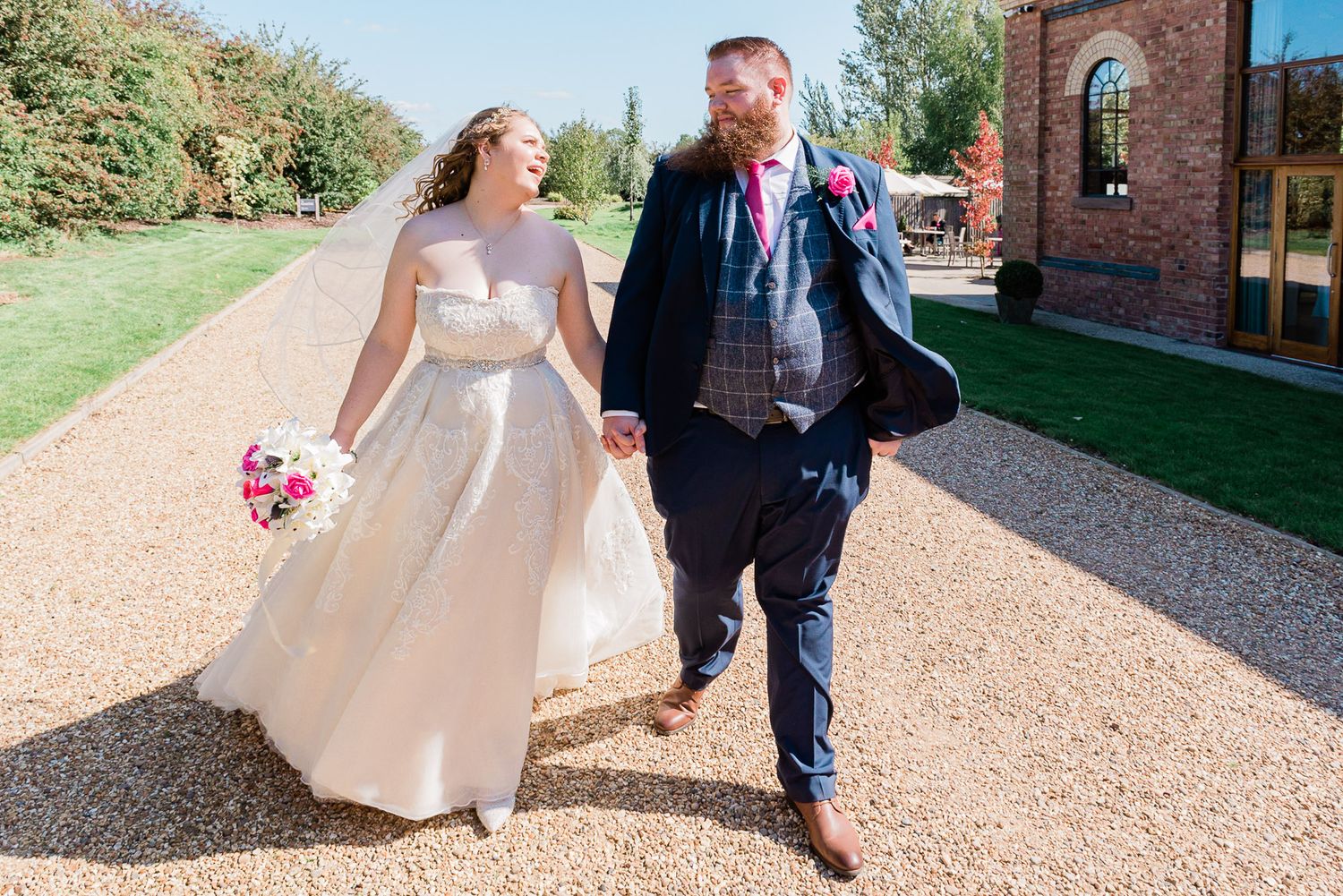 Bride and groom laugh and joke as they walk through the barn grounds