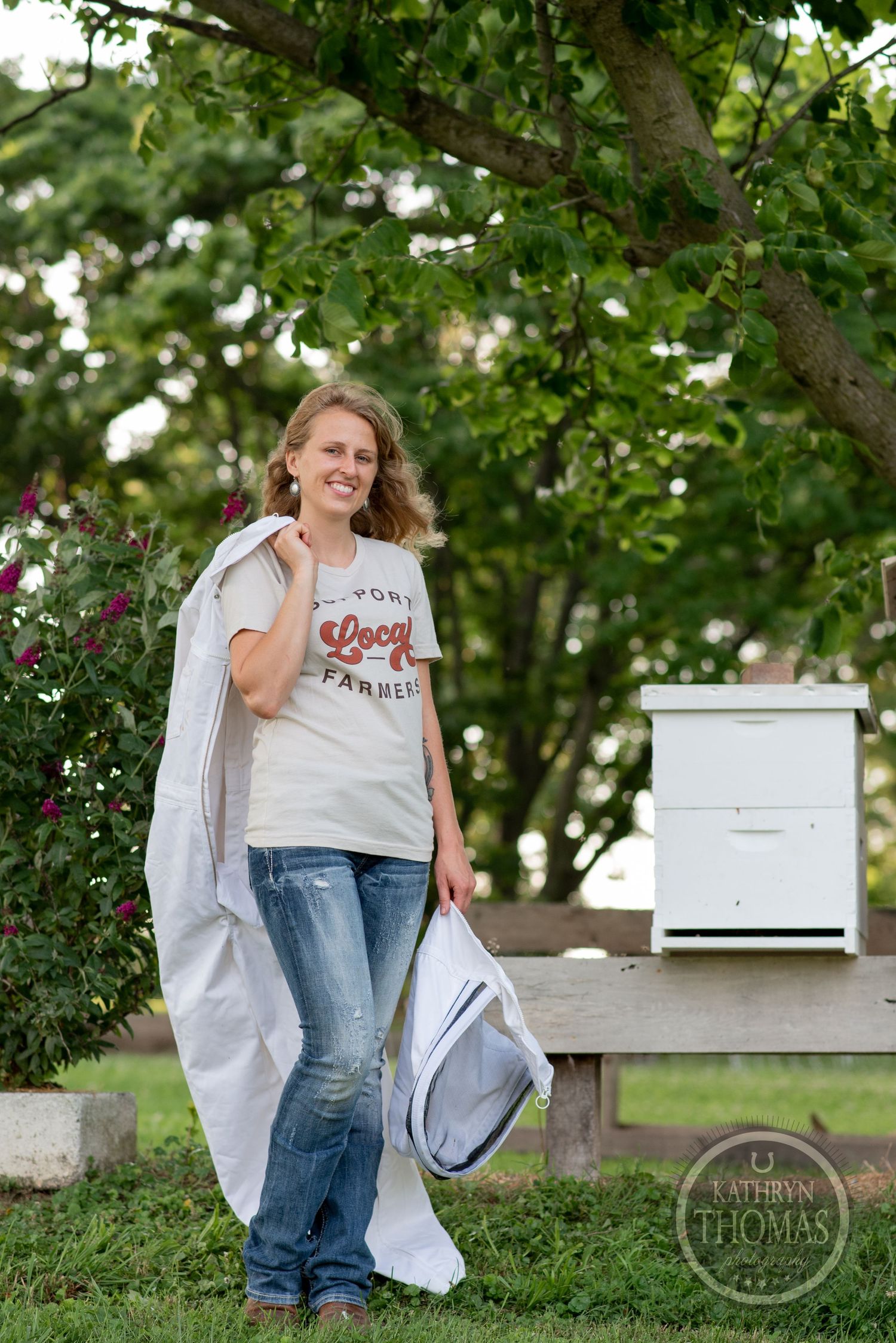 A relaxed rural setting with white beehive boxes and flowering bushes in the background.