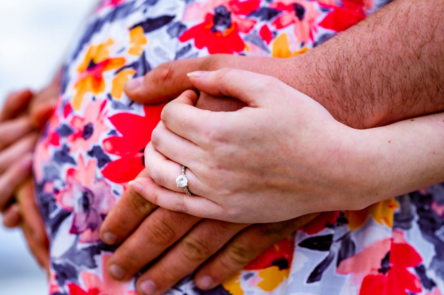 Close-up of hands resting on a floral dress with an engagement ring prominently displayed.