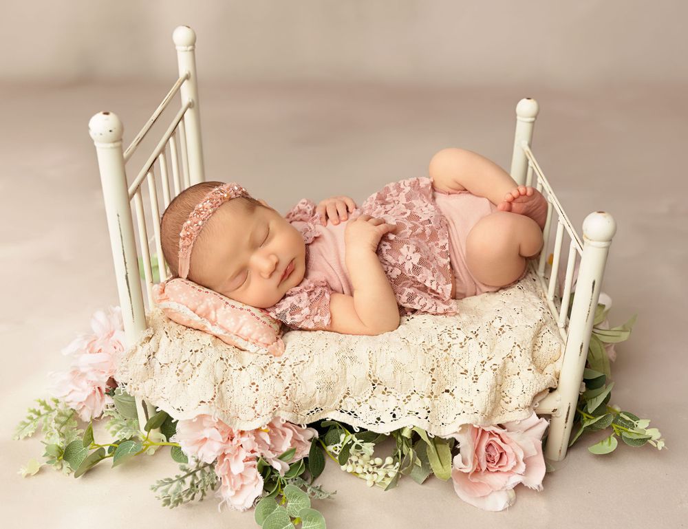 Sleeping newborn posed on a vintage bed with florals during a studio newborn session in Tilton NH